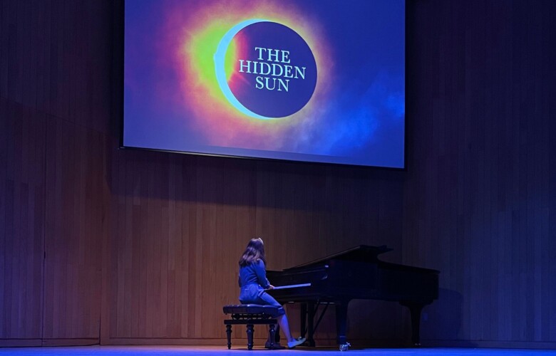 Person on stage playing piano with a Hidden Sun banner in the background