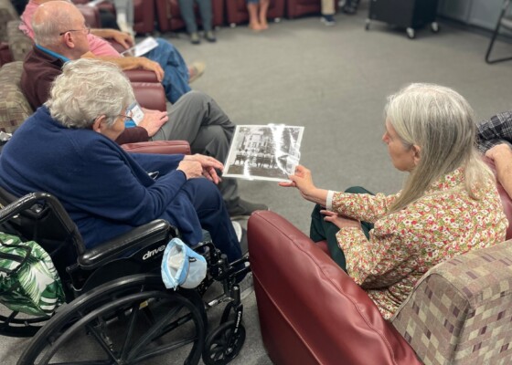 A person handing a historic photo to another person in a room with people sitting in a circle