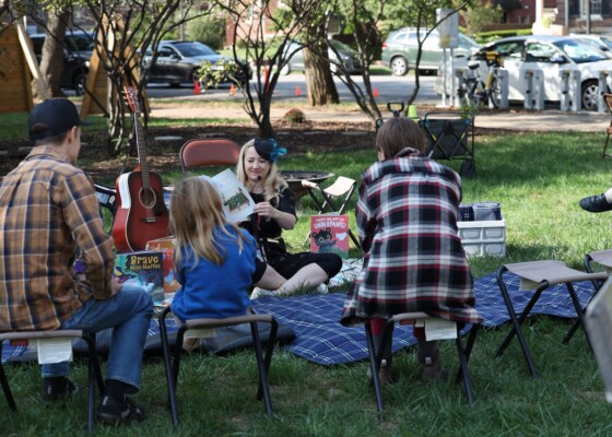 Woman reading to kids and parents on lawn